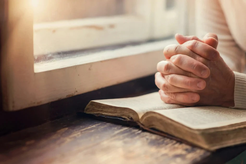 A woman with her hands clasped in prayer on an open bible